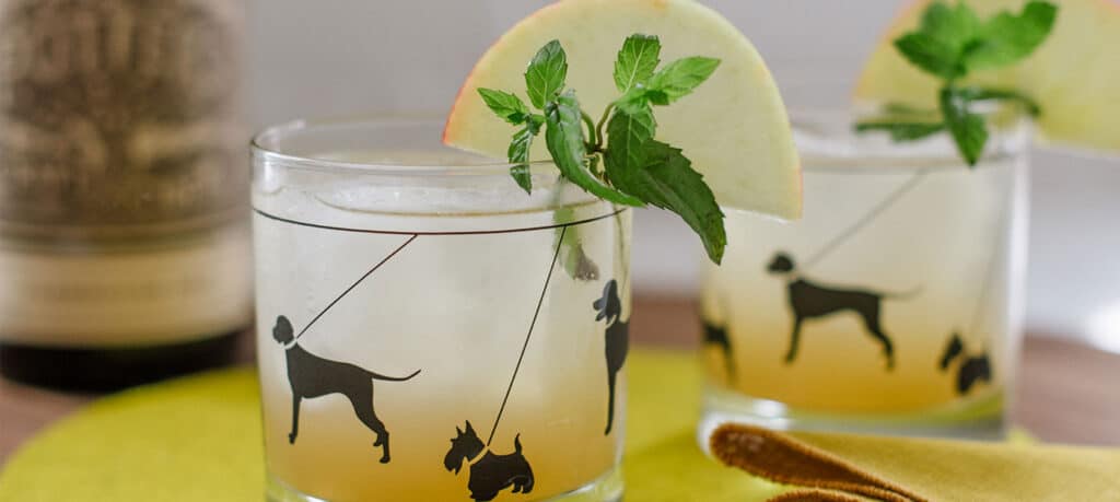Honey Bourbon Cider cocktail in a cocktail glass with black dogs, mint and lemon garnish