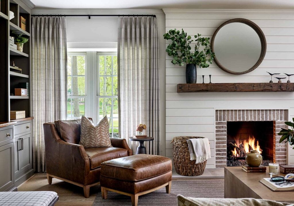 Photo of warm white living room with fireplace, bookshelves and leather armchair designed by Casey Sanford of Richmond Virginia