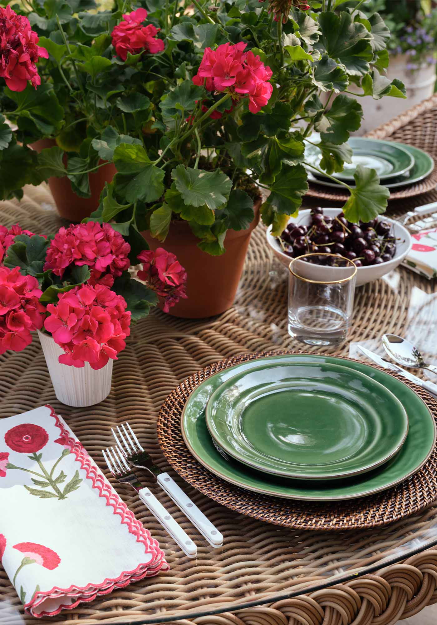 Close-up of the patio set tablescape at the 2025 Southern Living Idea House by Charlotte Moss, featuring elegant tableware, glassware, and potted geraniums.