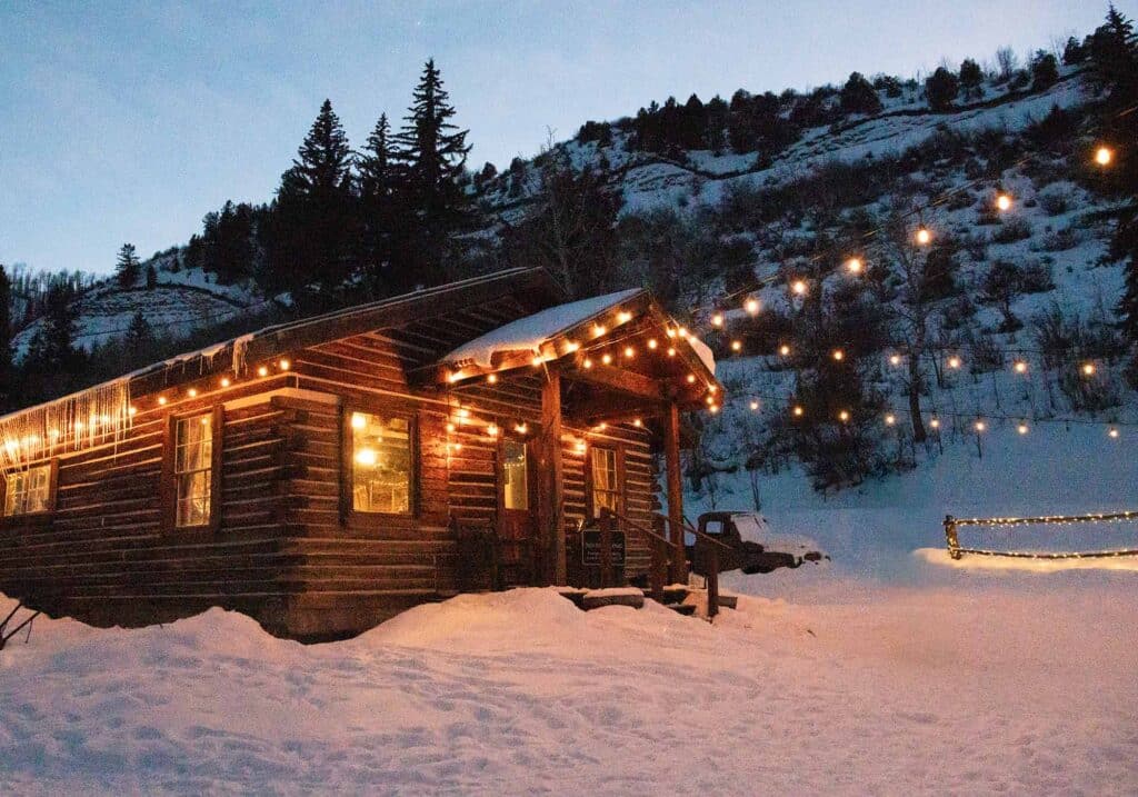 Snow-covered log cabin at Bearcat Stables, Vail, offering a cozy setting for winter sleigh rides and dining.