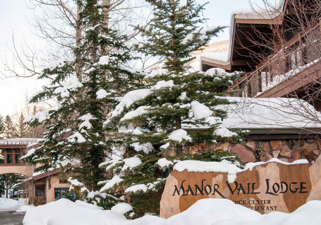 Front of Manor Vail Lodge surrounded by winter snow and mountain scenery in Vail Valley.
