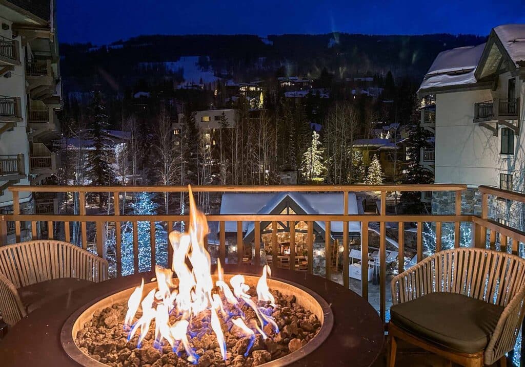 Balcony at a Vail resort with a lit fire table and scenic winter mountain landscape.