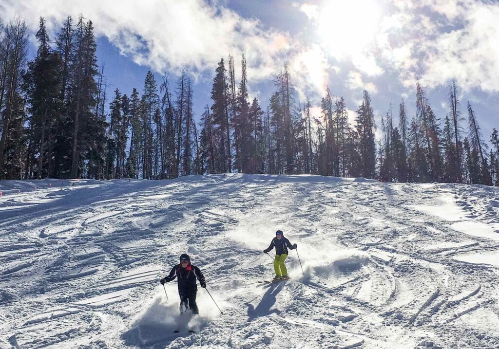 Winter sports enthusiasts skiing down Vail’s back bowls, surrounded by fresh snow and pine trees.