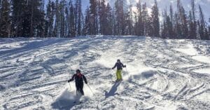 Skiers descending a powder-covered slope at Vail Resort, Colorado, with the sun reflecting on the mountains.