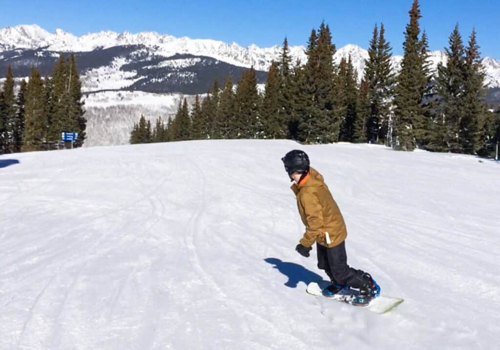 Snowboarder carving down a snow-covered slope at Vail Resort, Colorado, with mountain views in the background.
